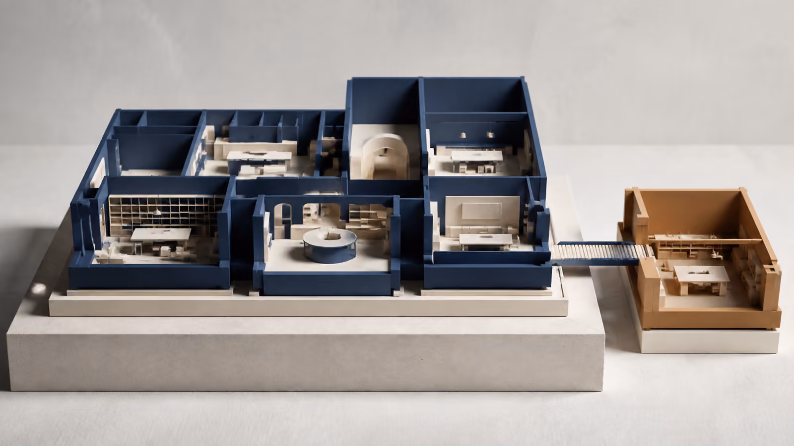 Architectural model with blue rooms on a shared foundation and a separate amber workshop connected by one bridge.